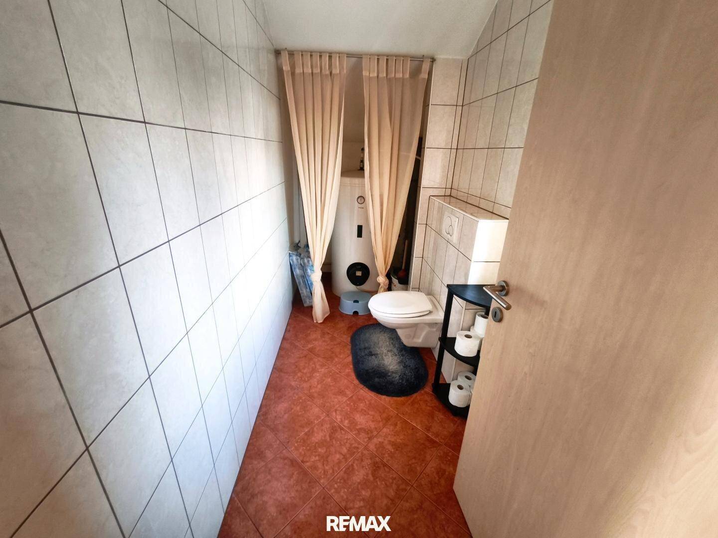 Einfaches WC mit Fliesenboden, Toilette und Warmwasserboiler.