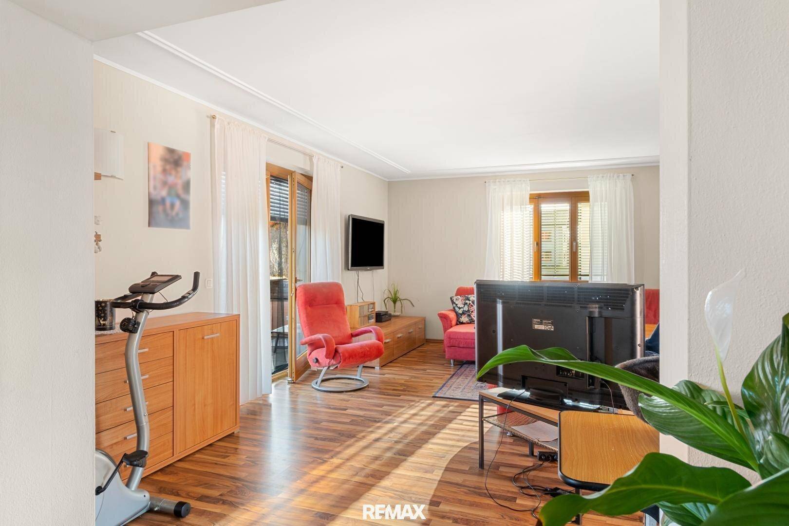 Gemütliches Wohnzimmer mit Holzboden, Zugang zum Balkon und bequemen roten Sesseln.