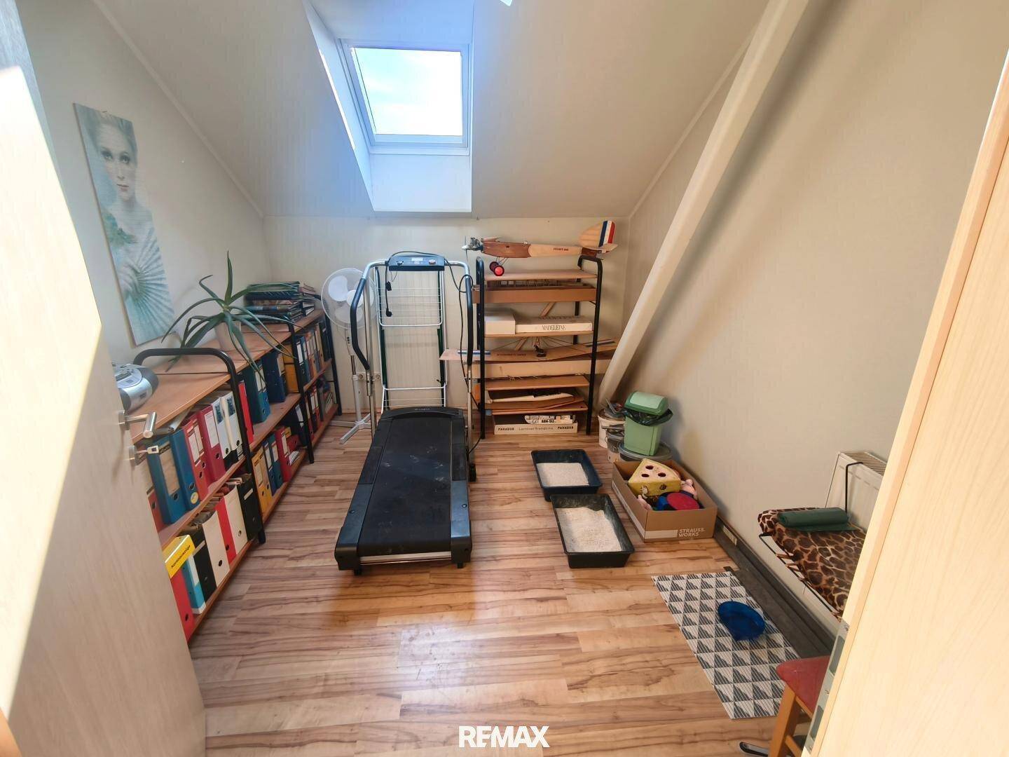 Kleines Zimmer im Dachgeschoss mit Laufband, Regalen und Dachfenster.