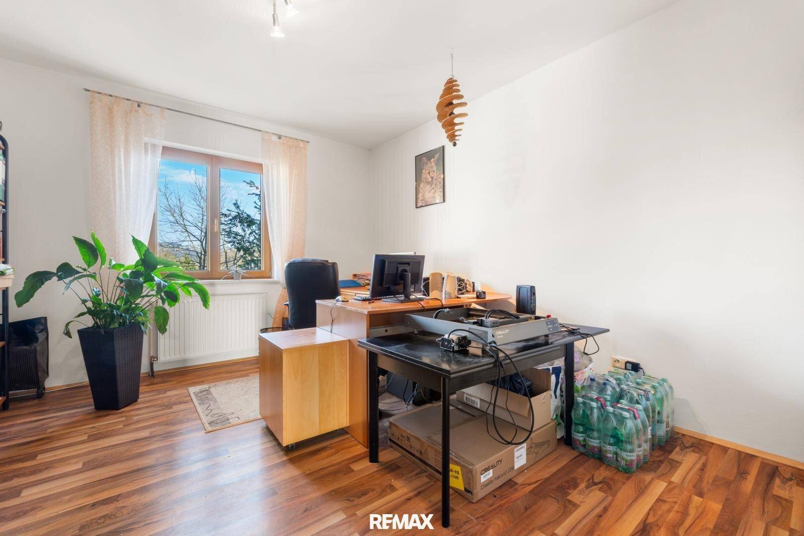 Arbeitszimmer mit Holzboden, großem Fenster und Blick ins Grüne, ausgestattet mit Schreibtisch.