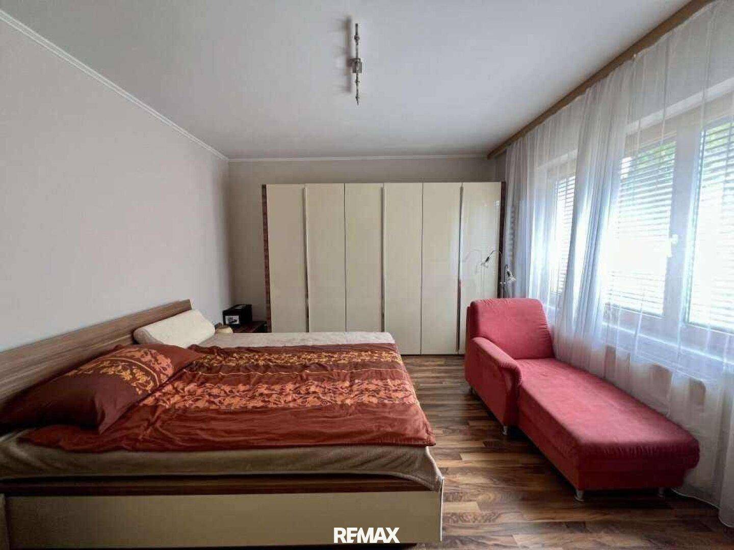 Schlafzimmer mit Holzboden, großem Kleiderschrank und einem bequemen Bett mit Tagesdecke.