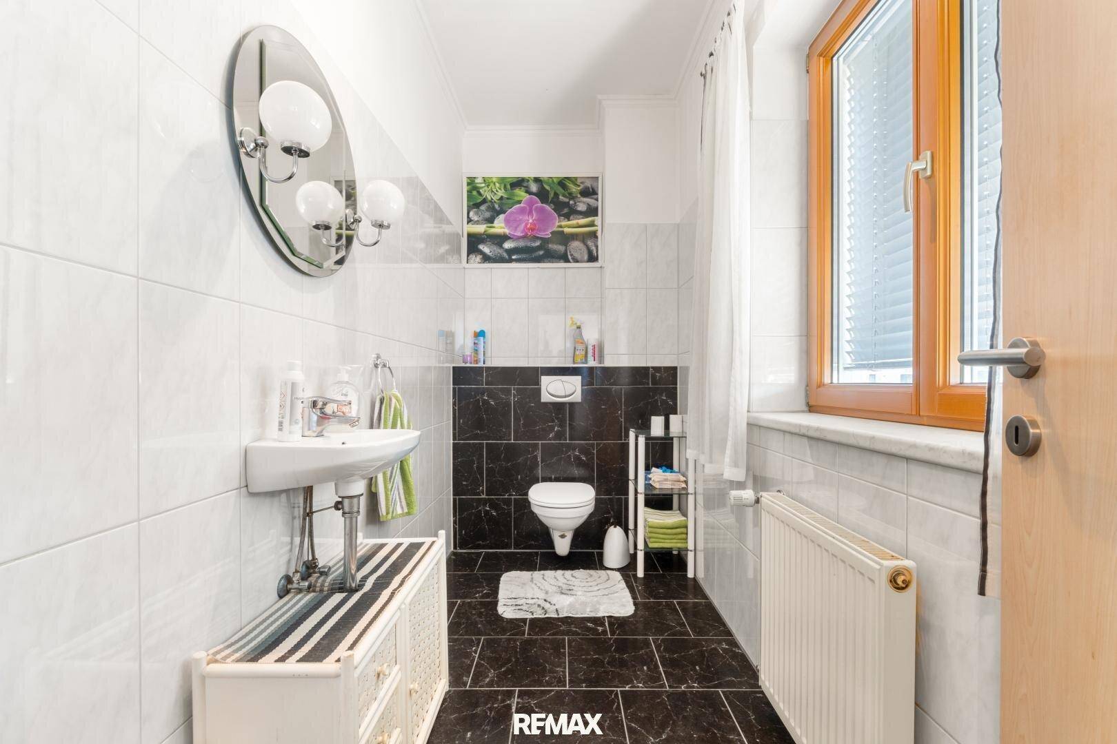Kleines Gäste-WC mit dunklen und weißen Fliesen, Waschbecken und Fenster.