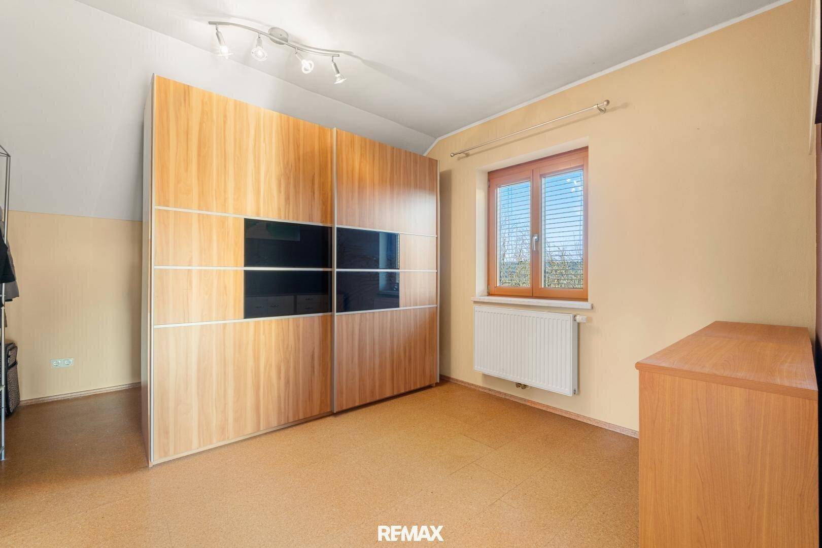 Schlafzimmer mit großem Einbauschrank, Fenster und Korkboden.