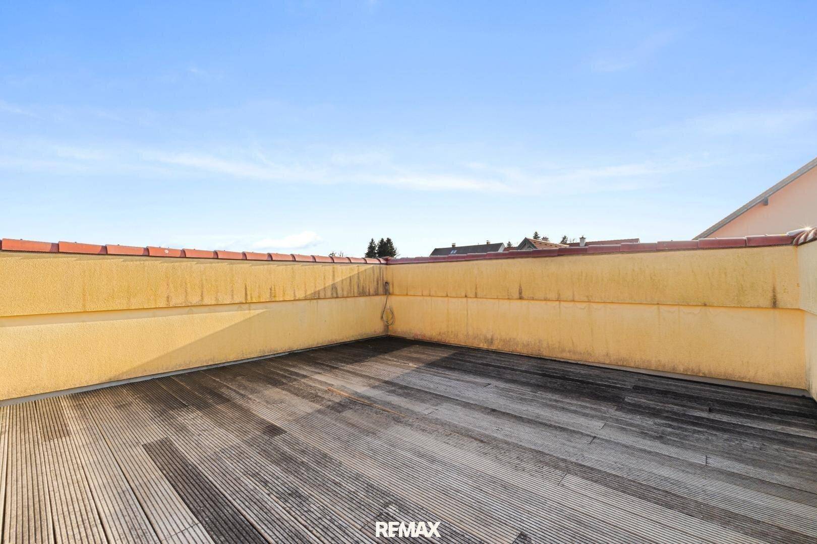 Große Dachterrasse mit Holzdielenboden und gelber Brüstung unter blauem Himmel.