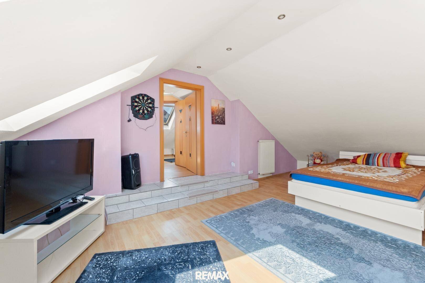 Gemütliches Schlafzimmer im Dachgeschoss mit Bett, Fernseher und Teppichen auf dem Holzboden.