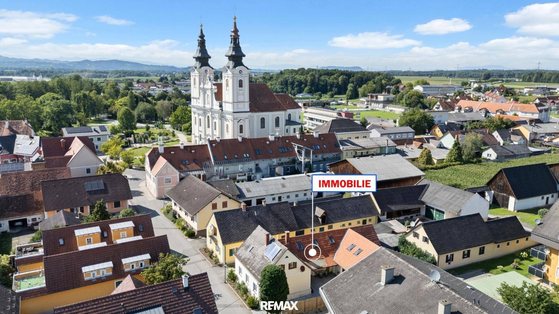 Luftaufnahme der Stadt mit der Immobilie im Zentrum und einer historischen Kirche im Hintergrund.