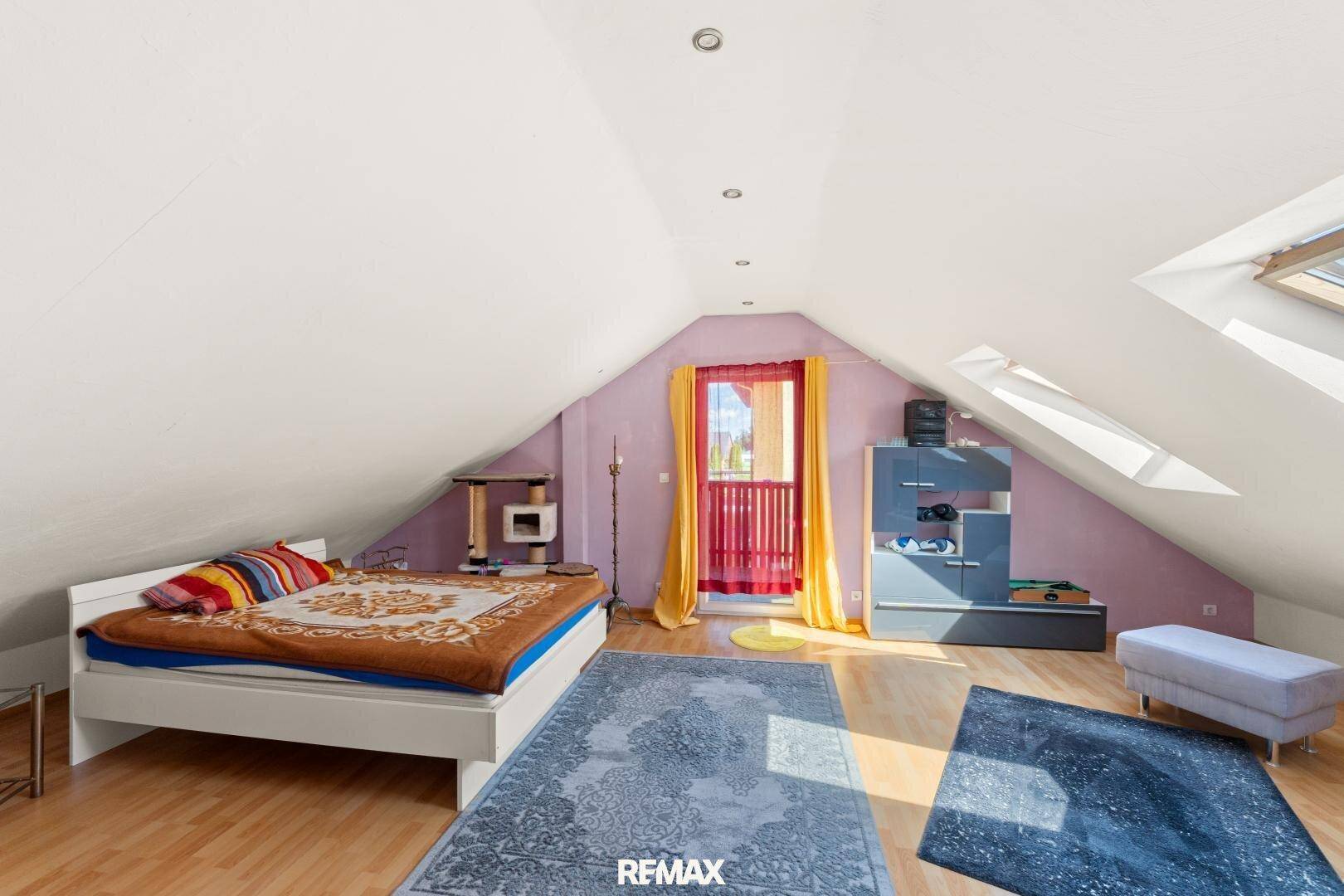 Schlafzimmer im Dachgeschoss mit Bett, Teppich und Dachfenstern für eine gemütliche Atmosphäre.