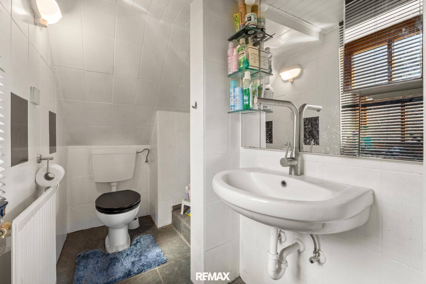 Kleines Badezimmer mit Dachschräge, WC, Waschbecken und Fenster für Tageslicht.