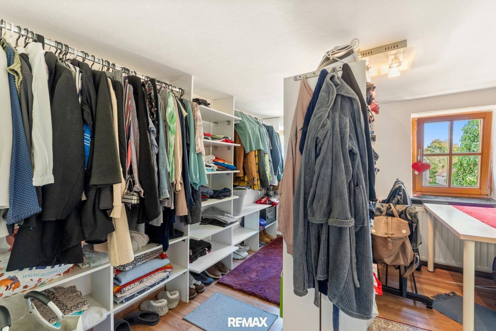 Begehbarer Kleiderschrank mit Regalen, Kleiderstangen und Fenster für natürliche Belichtung.