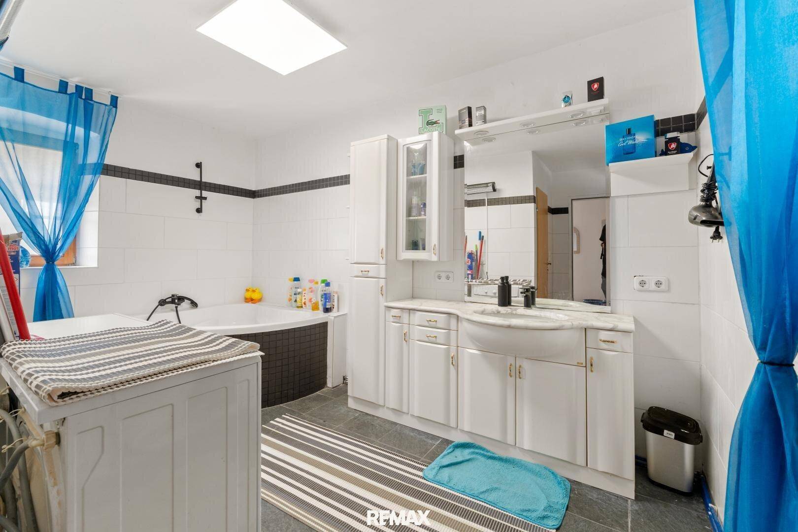 Geräumiges Badezimmer mit Eckbadewanne, Doppelwaschbecken und blauen Vorhängen am Fenster.