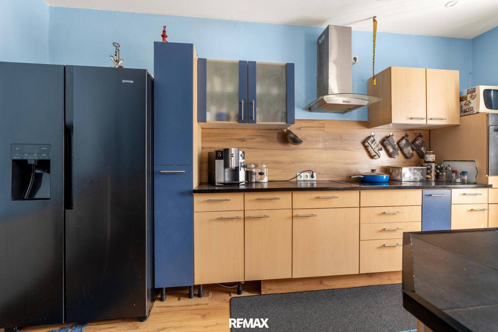 Funktionale Küche mit Holzfronten, schwarzem Kühlschrank und Dunstabzugshaube über dem Kochbereich.
