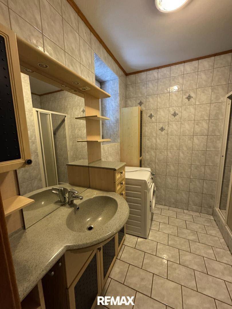 Gefliestes Badezimmer mit Waschbecken, Spiegelschrank und einer Waschmaschine.