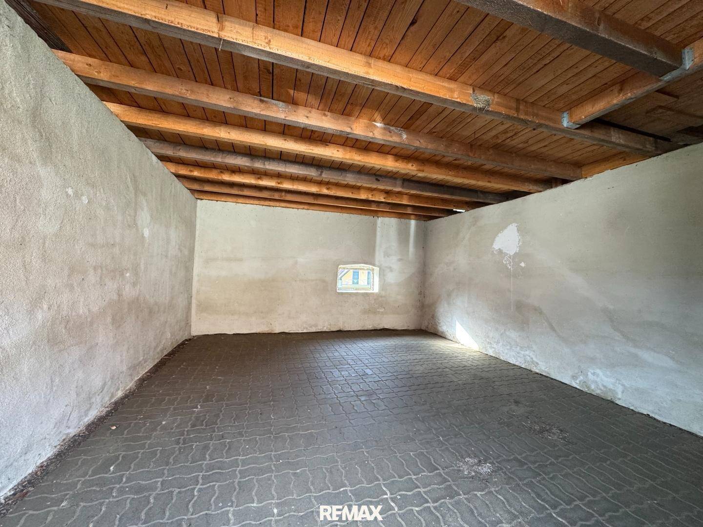 Unfertiger Raum mit sichtbaren Holzbalken an der Decke und Betonboden, nutzbar als Abstellraum.
