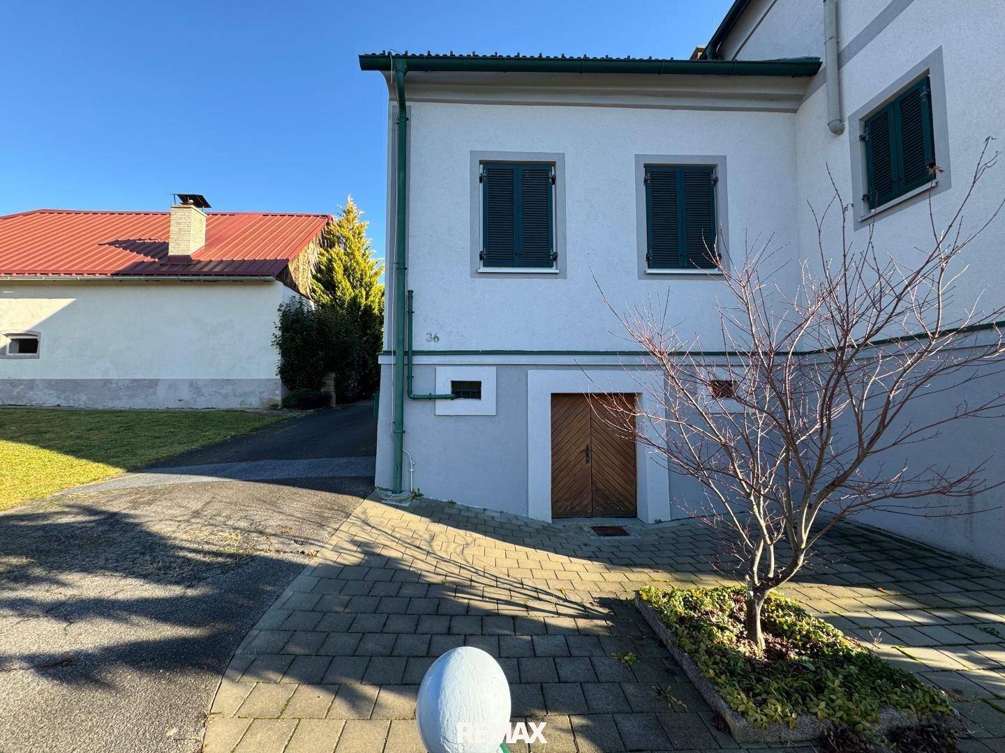 Seitenansicht des Hauses mit gepflastertem Zugang und einem jungen Baum im Vordergrund.