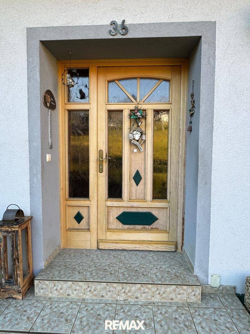 Hölzerne Eingangstür mit Glaseinsätzen und dekorativen Elementen, umgeben von einem grauen Rahmen.
