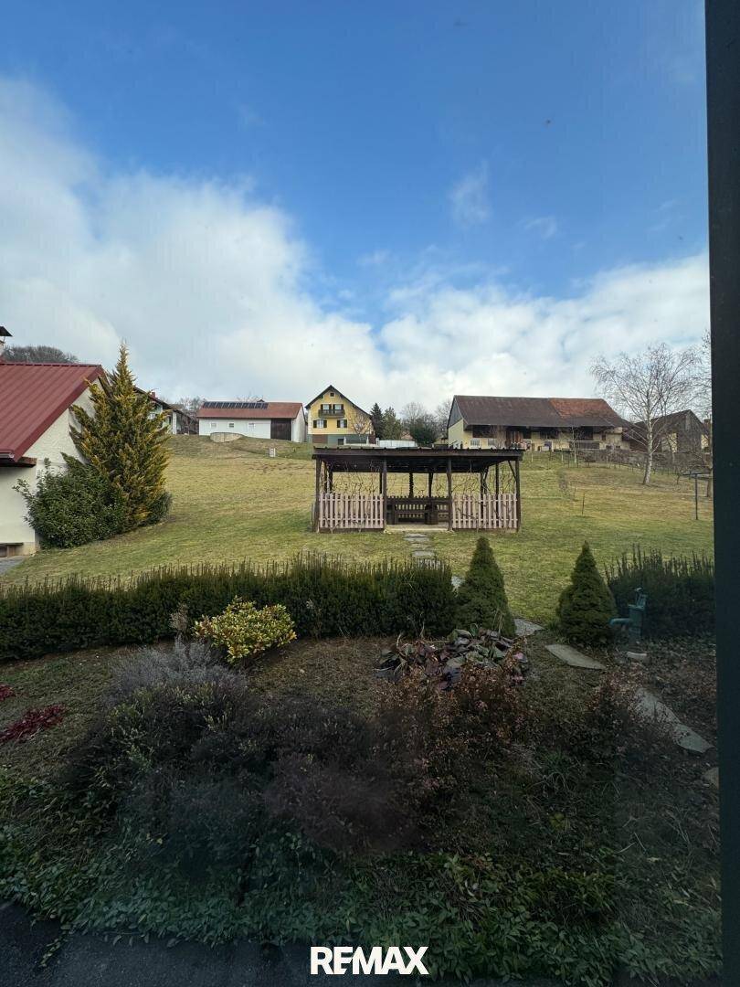Blick aus dem Fenster auf den grünen Garten mit Pavillon und die umliegende Landschaft.