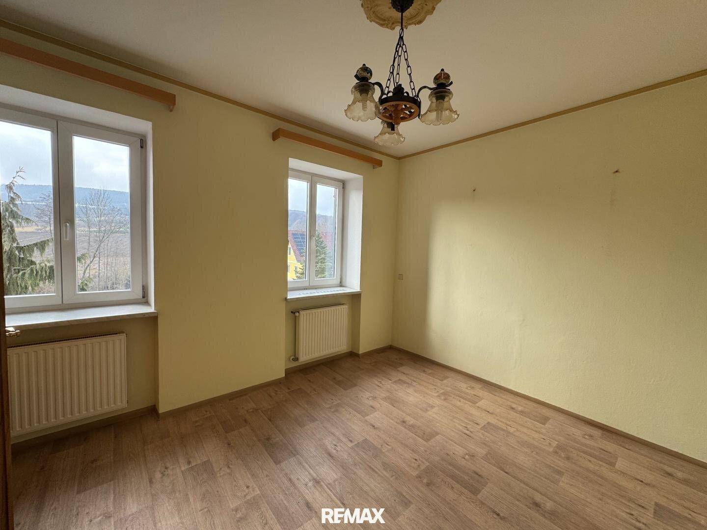 Heller Raum mit Laminatboden, Fenstern und Heizkörpern, bereit zur individuellen Gestaltung.