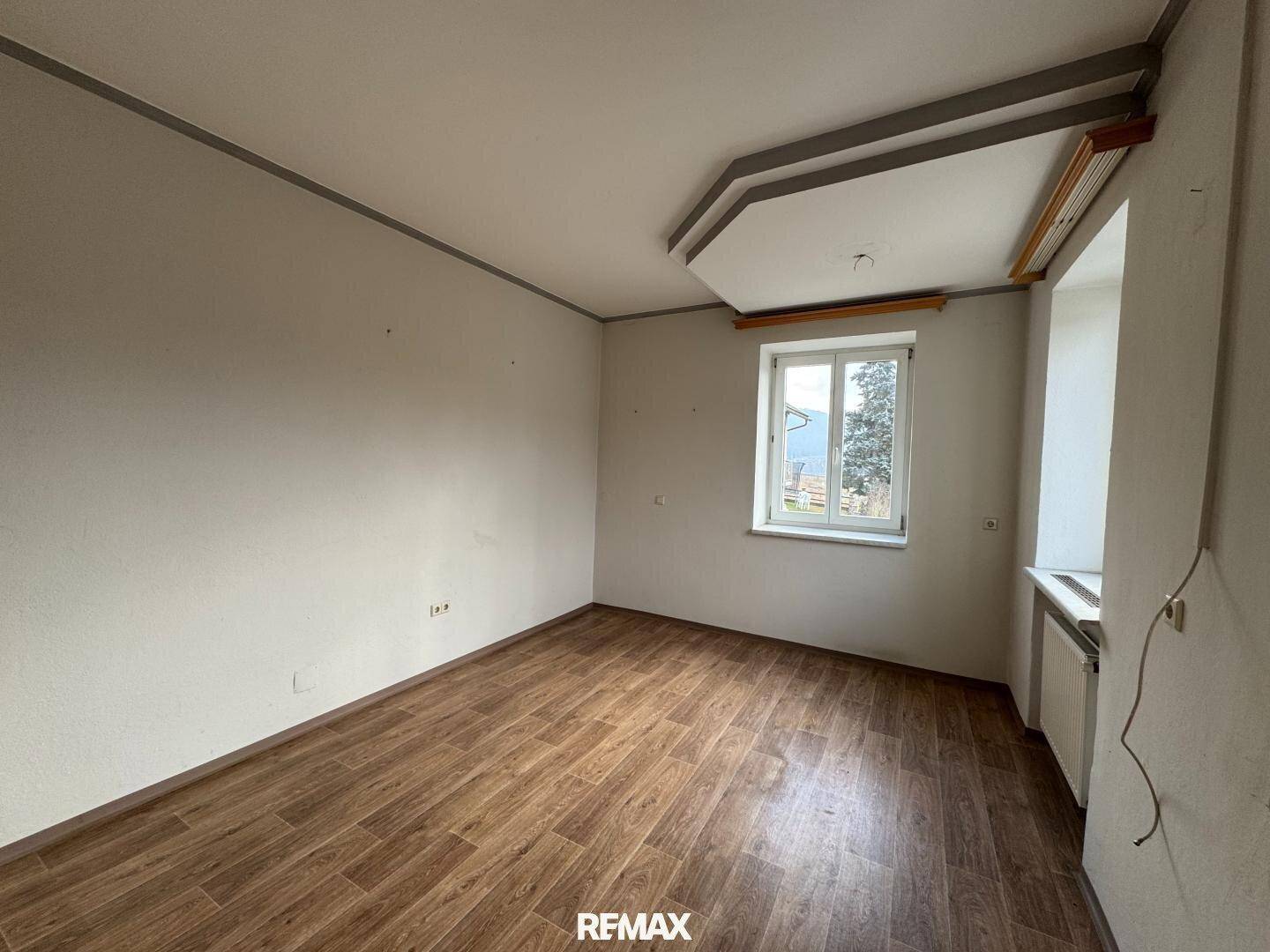 Leerer Raum mit Laminatboden, hellen Wänden und einem Fenster mit Blick nach draußen.