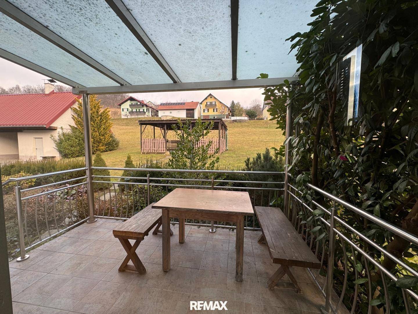 Überdachte Terrasse mit Holztisch und Bänken, ideal für Mahlzeiten im Freien mit Blick auf die Landschaft.