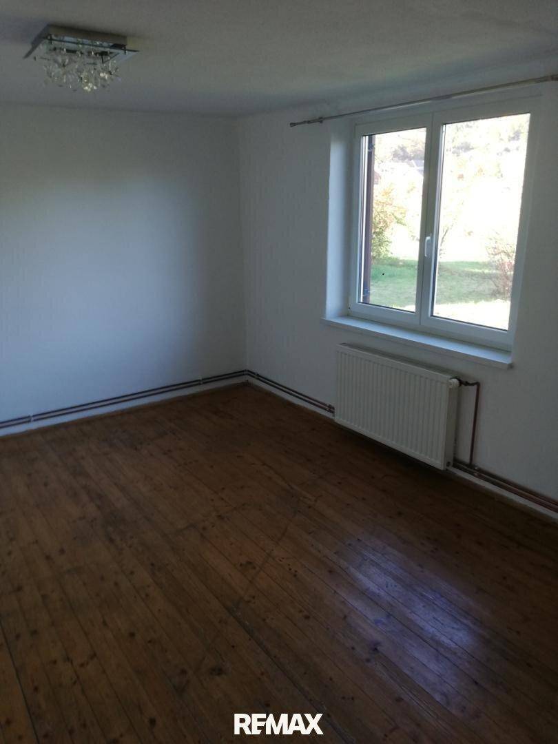 Helles Zimmer mit Holzdielenboden, weißen Wänden und einem großen Fenster, das viel Tageslicht hereinlässt.