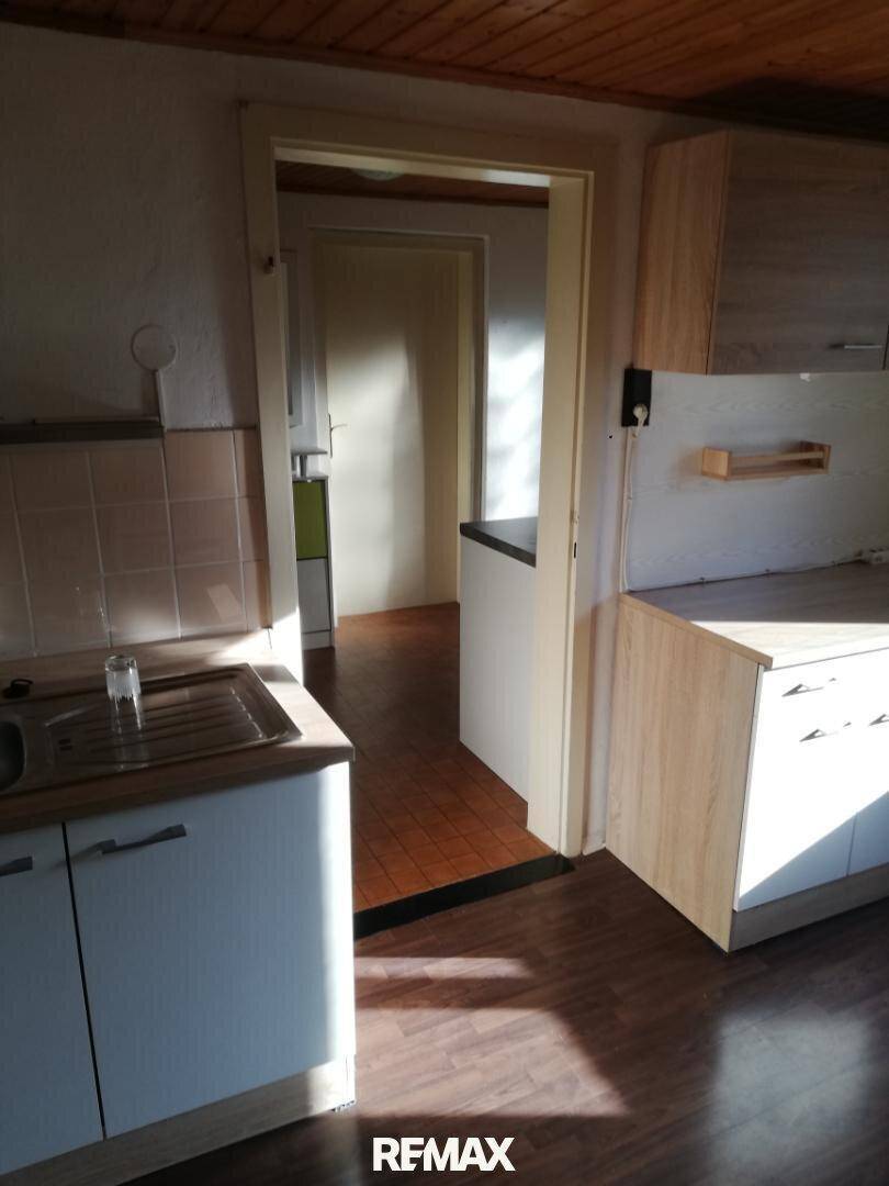 Küchenzeile mit Spüle, gefliestem Spritzschutz und Holzschränken, die in einen weiteren Raum führt.