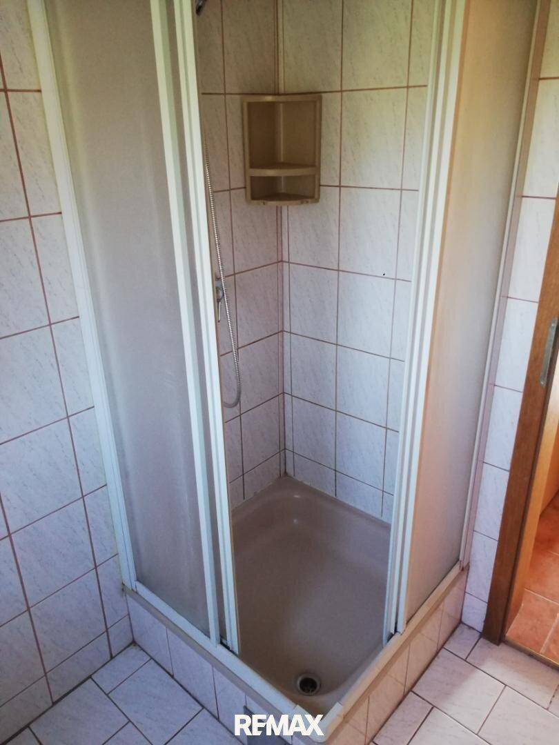Duschkabine in einem Badezimmer mit hellen Fliesen an Wänden und Boden.