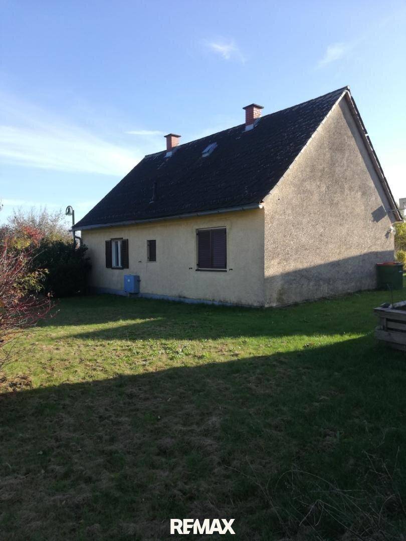 Seitenansicht eines Einfamilienhauses mit verputzter Fassade und Satteldach, umgeben von einer Rasenfläche.