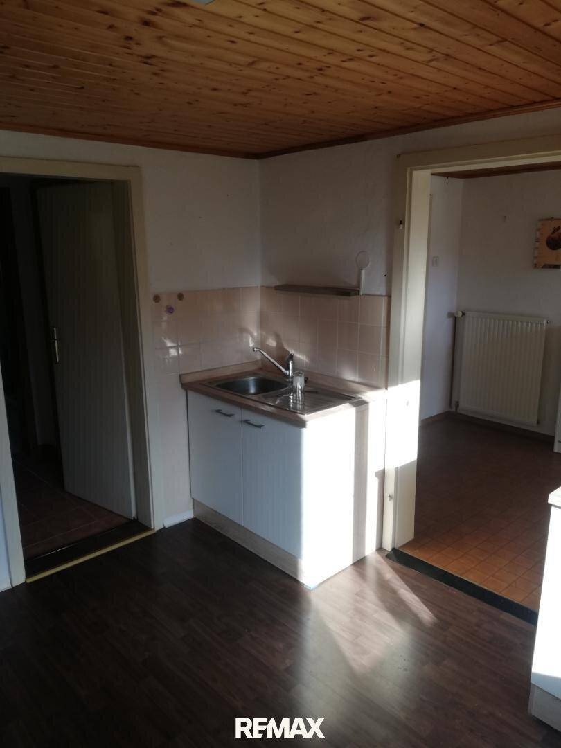 Einfache Küchenzeile mit Spülbecken und Holzschränken unter einer Holzdeckenverkleidung.