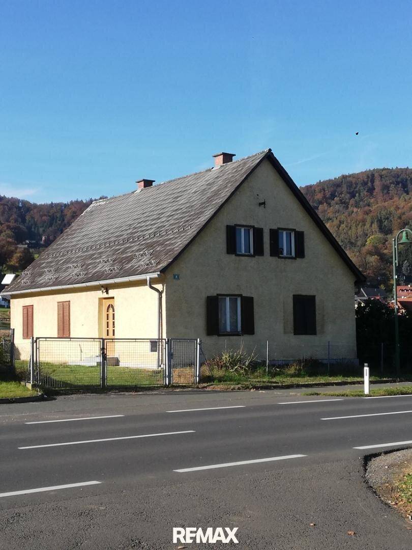 Vorderansicht des Hauses von der Straße aus, mit Fensterläden und einem Zaun, umgeben von ländlicher Umgebung.