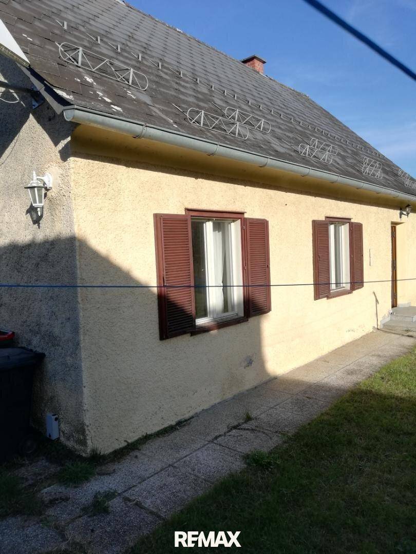 Seitenansicht des Hauses mit braunen Fensterläden und einer Außenleuchte, umgeben von Grünfläche.