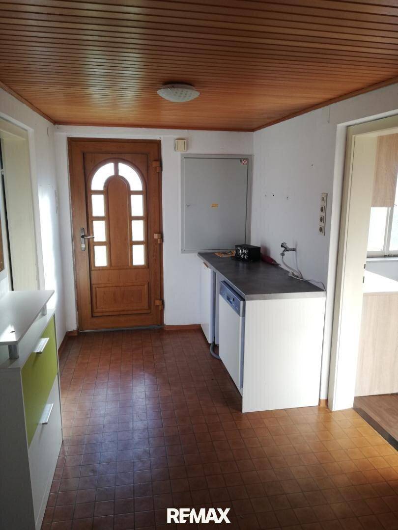 Eingangsbereich mit Holztür, gefliestem Boden und einer kleinen Arbeitsfläche mit Spülbecken.