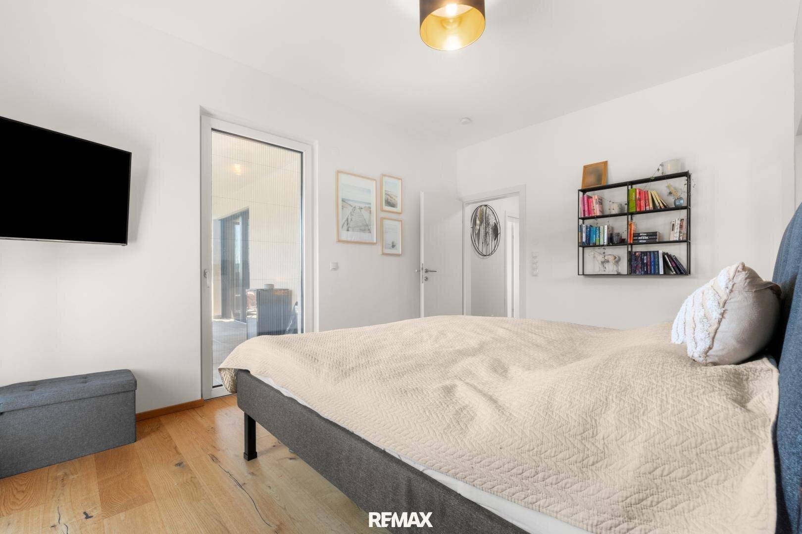 Schlafzimmer mit großem Bett, Holzboden und Zugang zu einem Außenbereich.