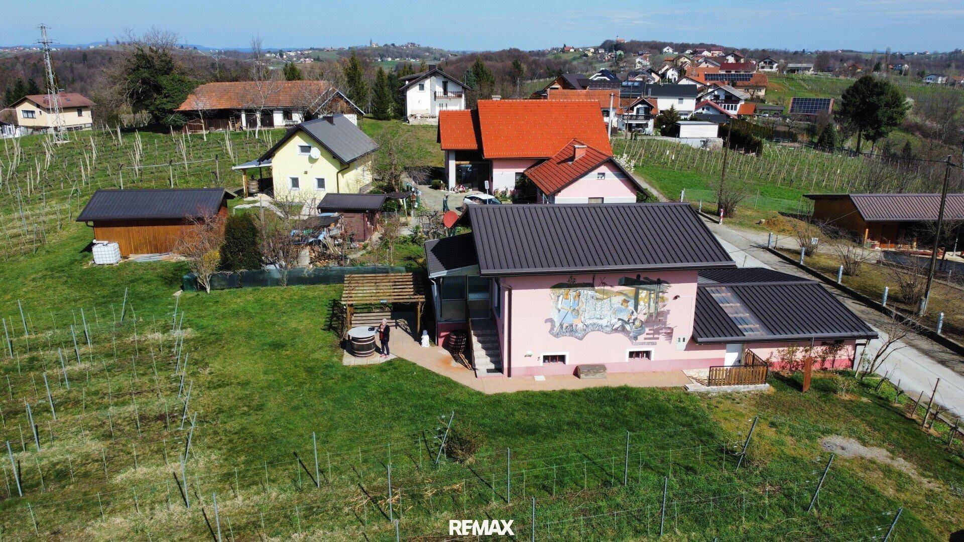 Rosa Haus mit dunklem Dach, umgeben von einem gepflegten Garten und Weinreben.