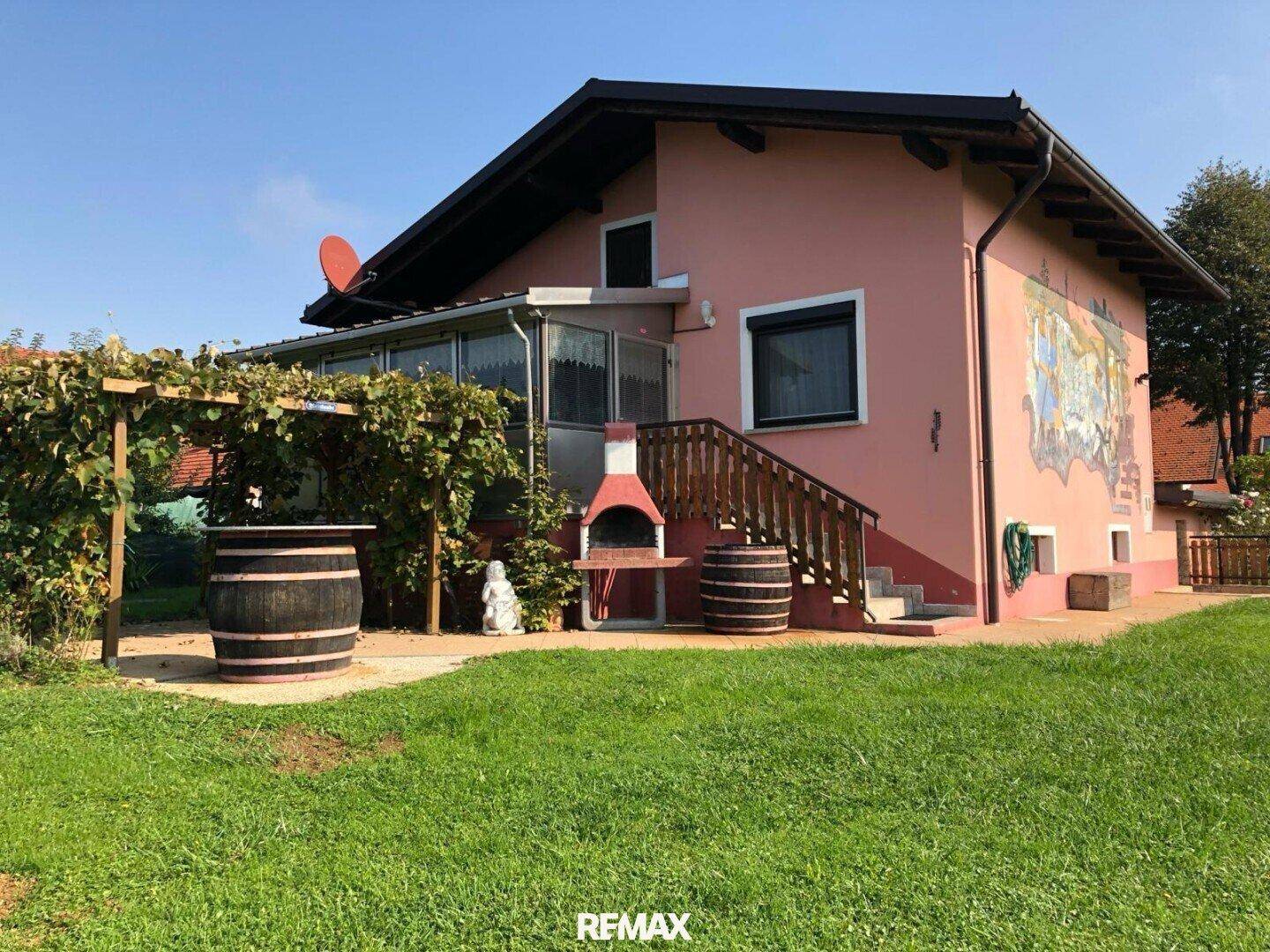 Außenbereich des Hauses mit Pergola, Weinfässern und einem Grillplatz im grünen Garten.