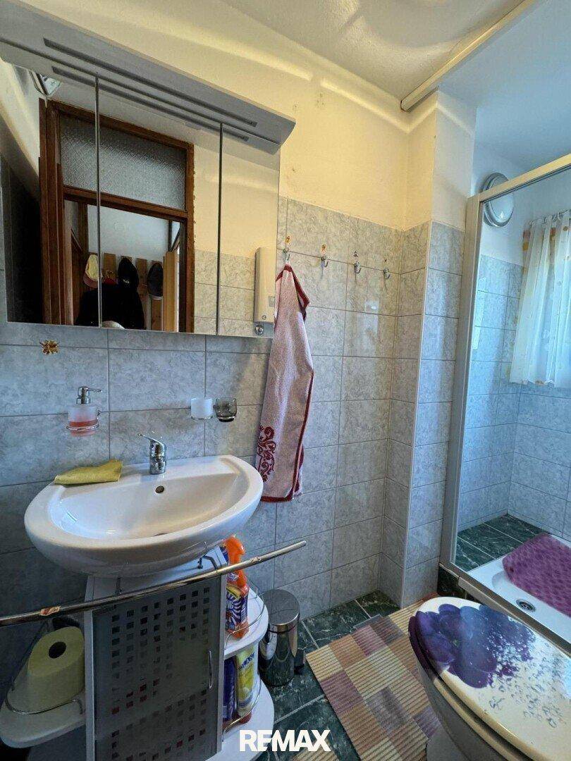 Badezimmer mit Waschbecken, Spiegel und Duschkabine, hell gefliest und funktional.