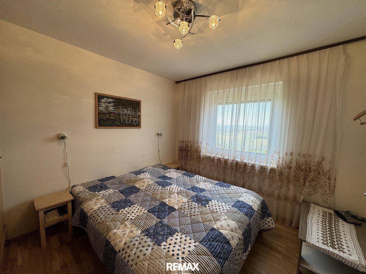 Schlafzimmer mit Doppelbett, Holzboden und großem Fenster mit Blick ins Grüne.