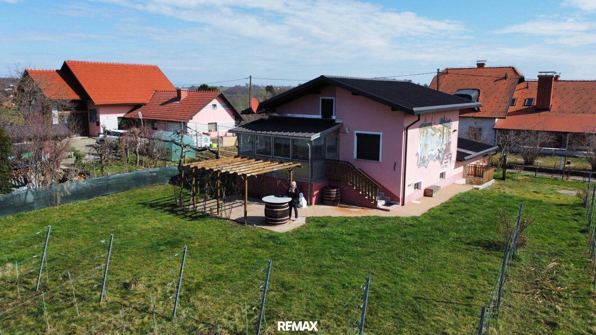 Rosa gestrichenes Haus mit Pergola und Gartenbereich in einer sonnigen ländlichen Umgebung.