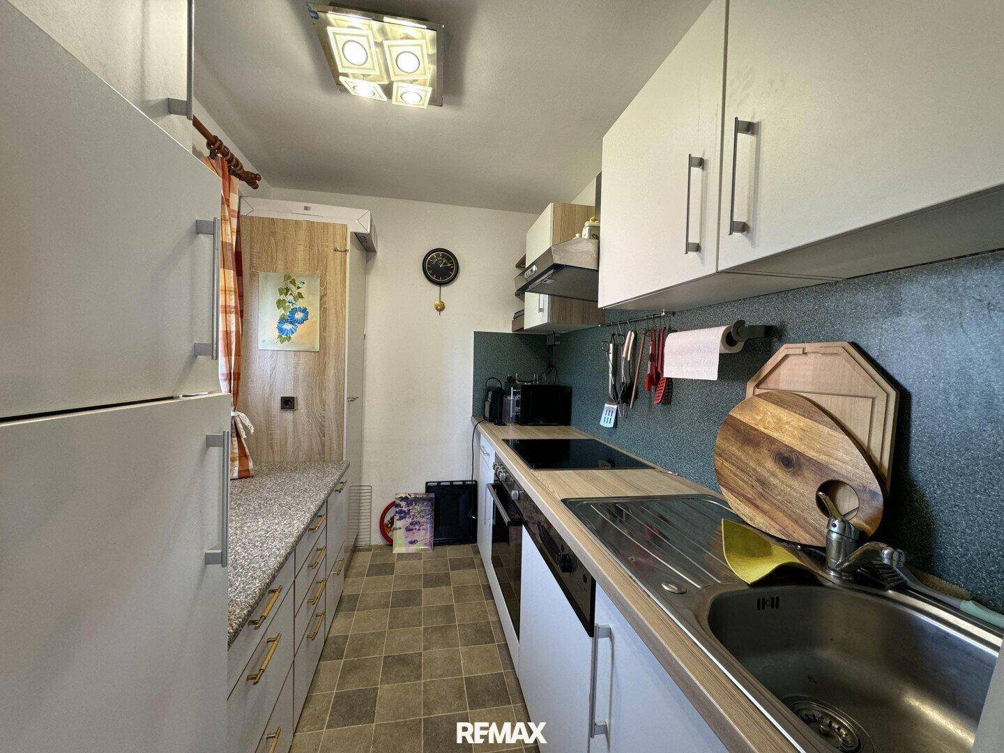 Schmale Küche mit weißen Schränken, Holztheke und Fliesenboden in funktionalem Design.