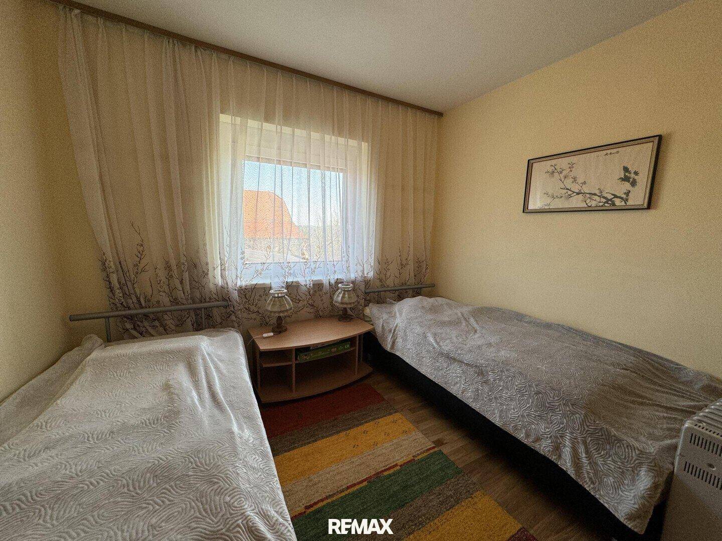 Schlafzimmer mit zwei Einzelbetten, Holzboden und Fenster mit Vorhängen.