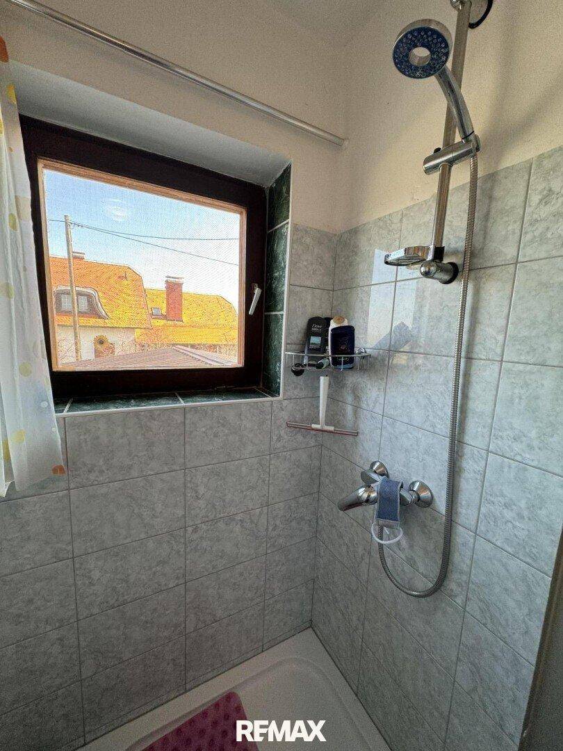 Badezimmer mit hellgrauen Fliesen, Duschwanne und Fenster, einfach und funktional.