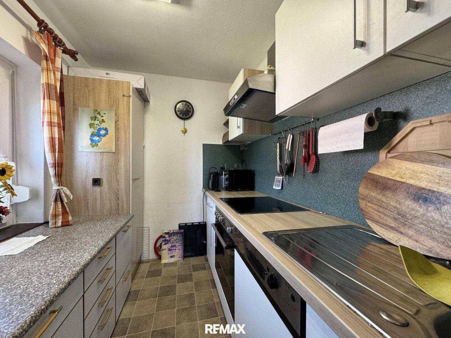 Funktionale Küche mit weißen Oberschränken, Holztheke und Fliesenboden, gut beleuchtet.