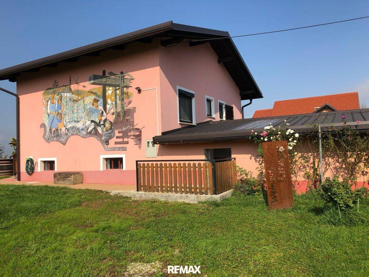 Rosa Hausfassade mit einem Wandgemälde und einem gepflegten Rasen im Vordergrund.