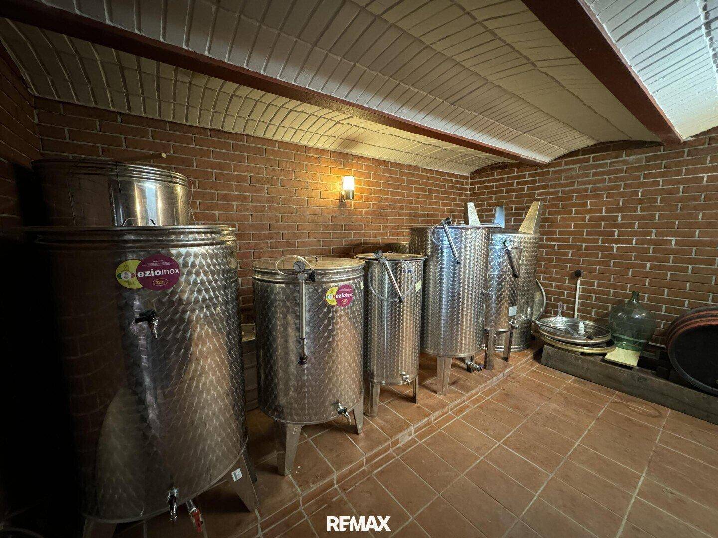 Weinkeller mit Ziegelwänden, Fliesenboden und mehreren Edelstahltanks zur Weinproduktion.