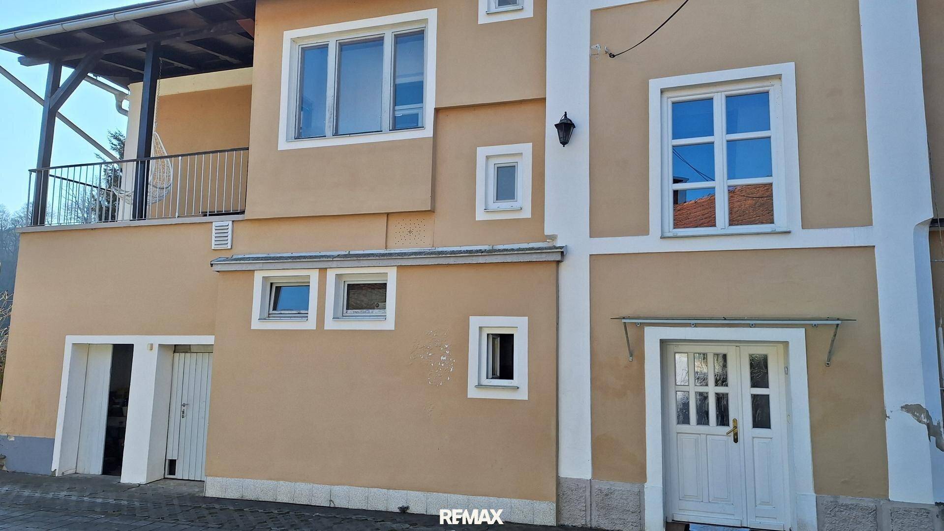 Nahaufnahme der Seitenfassade mit Eingangstür, Fenstern und einem überdachten Balkon.