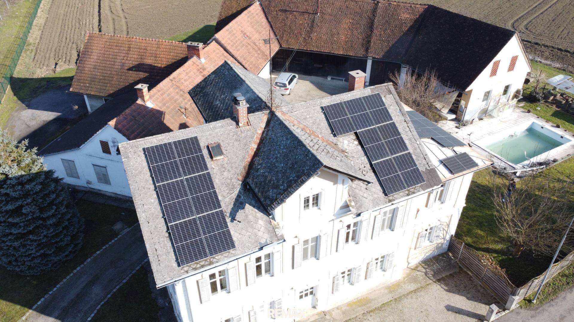 Detailreiche Luftaufnahme des Hauptgebäudes mit zahlreichen Solarmodulen auf dem Dach.