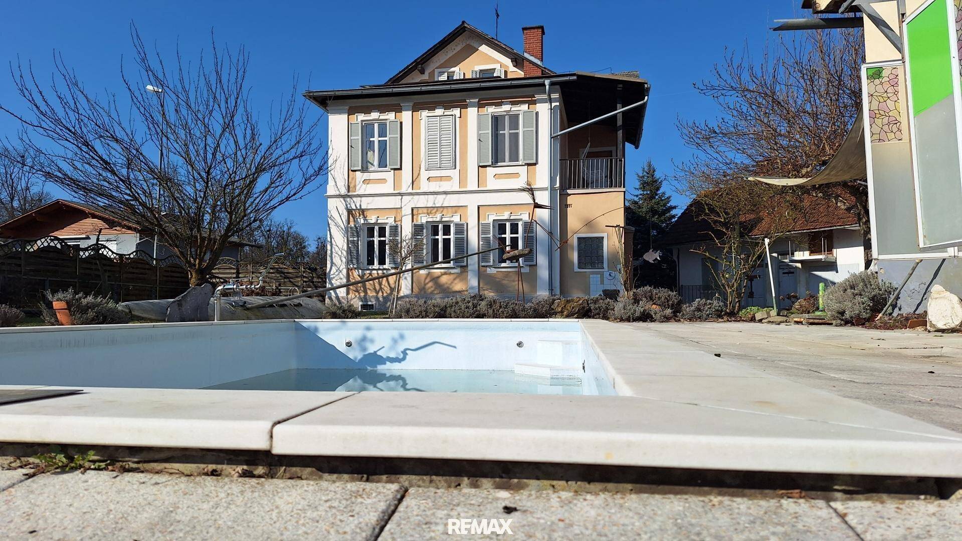Außenansicht des Hauses mit einem eingelassenen Swimmingpool im Vordergrund unter blauem Himmel.