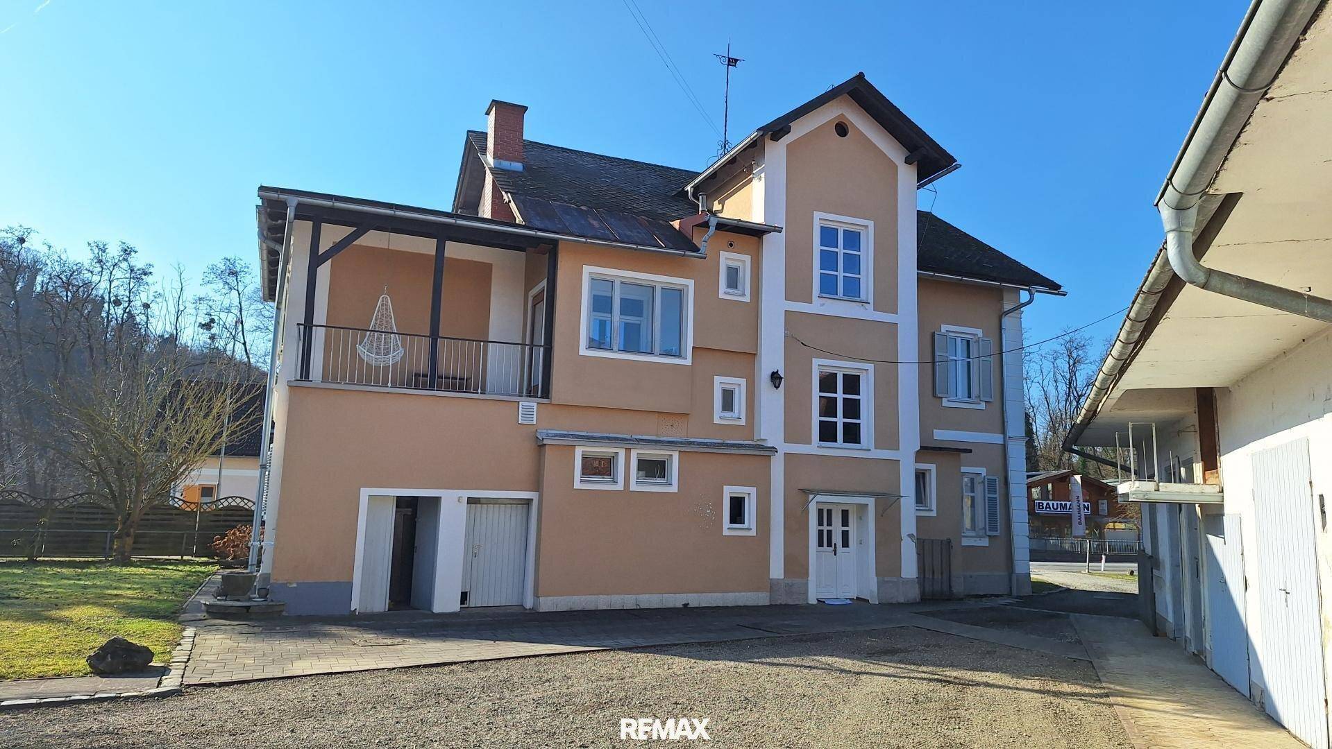 Rückseite des Gebäudes mit Zufahrt, überdachtem Balkon und angrenzendem Grünbereich.