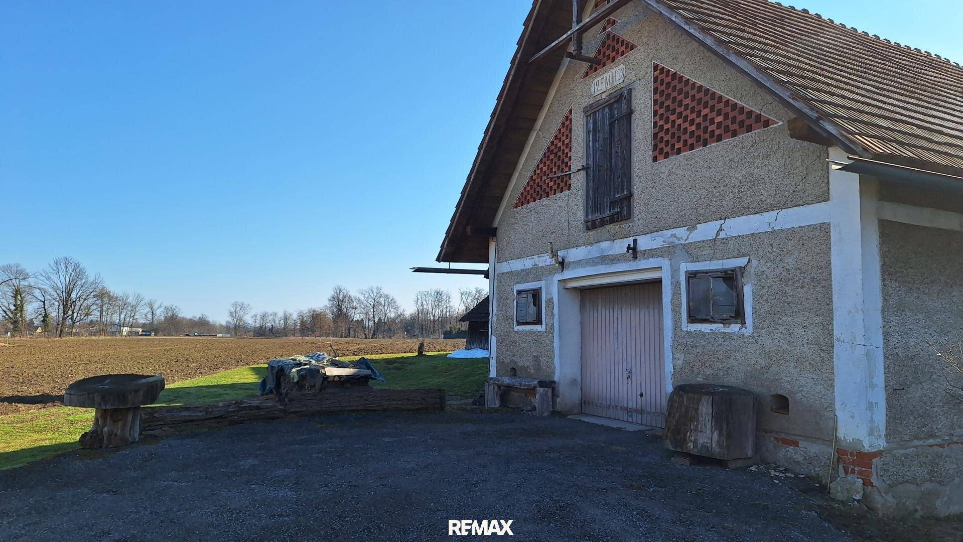 Altes Nebengebäude oder Scheune neben einem Feld unter strahlend blauem Himmel.