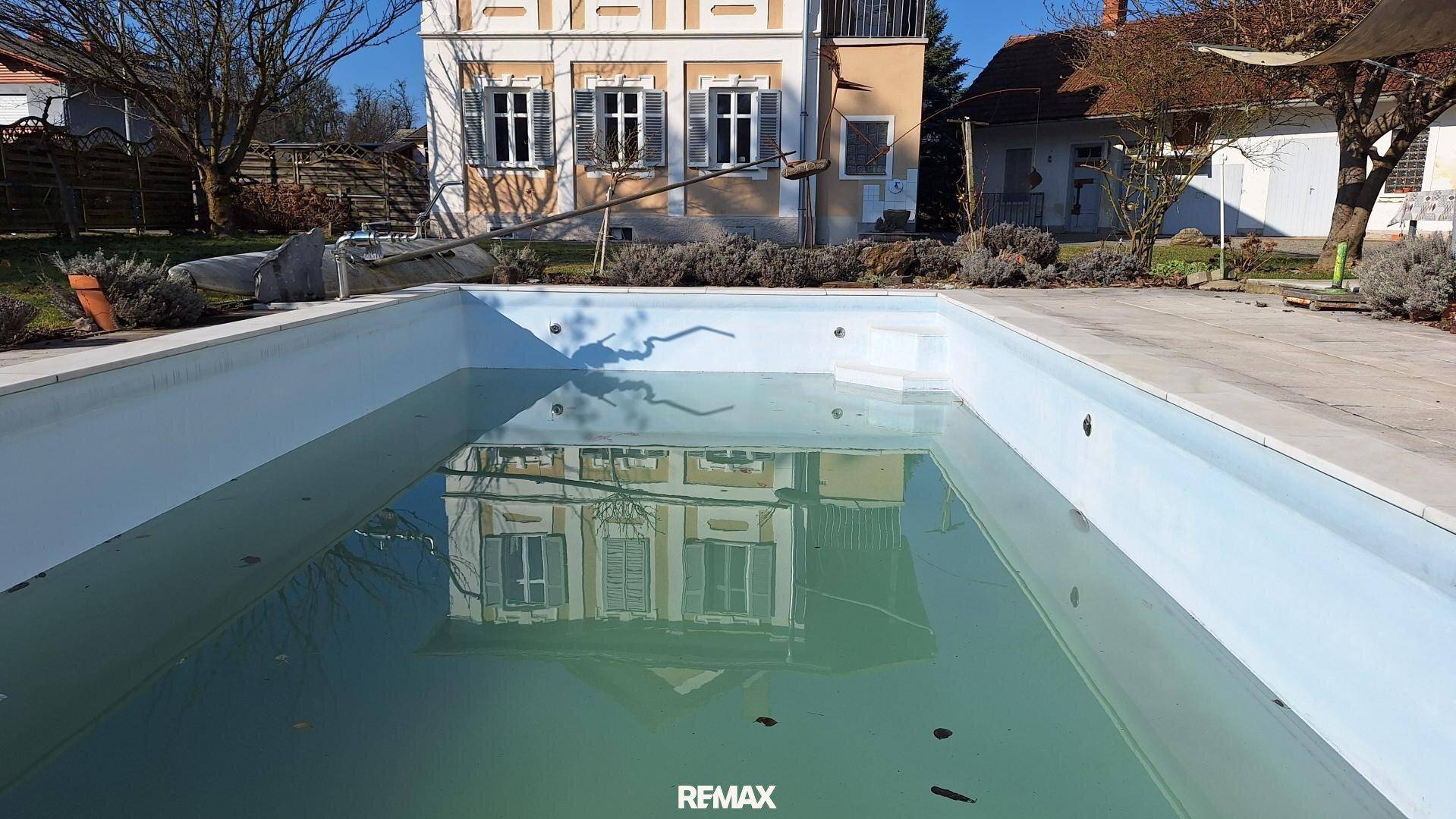 Außenpool mit der Spiegelung des Hauses im Wasser an einem sonnigen Tag.