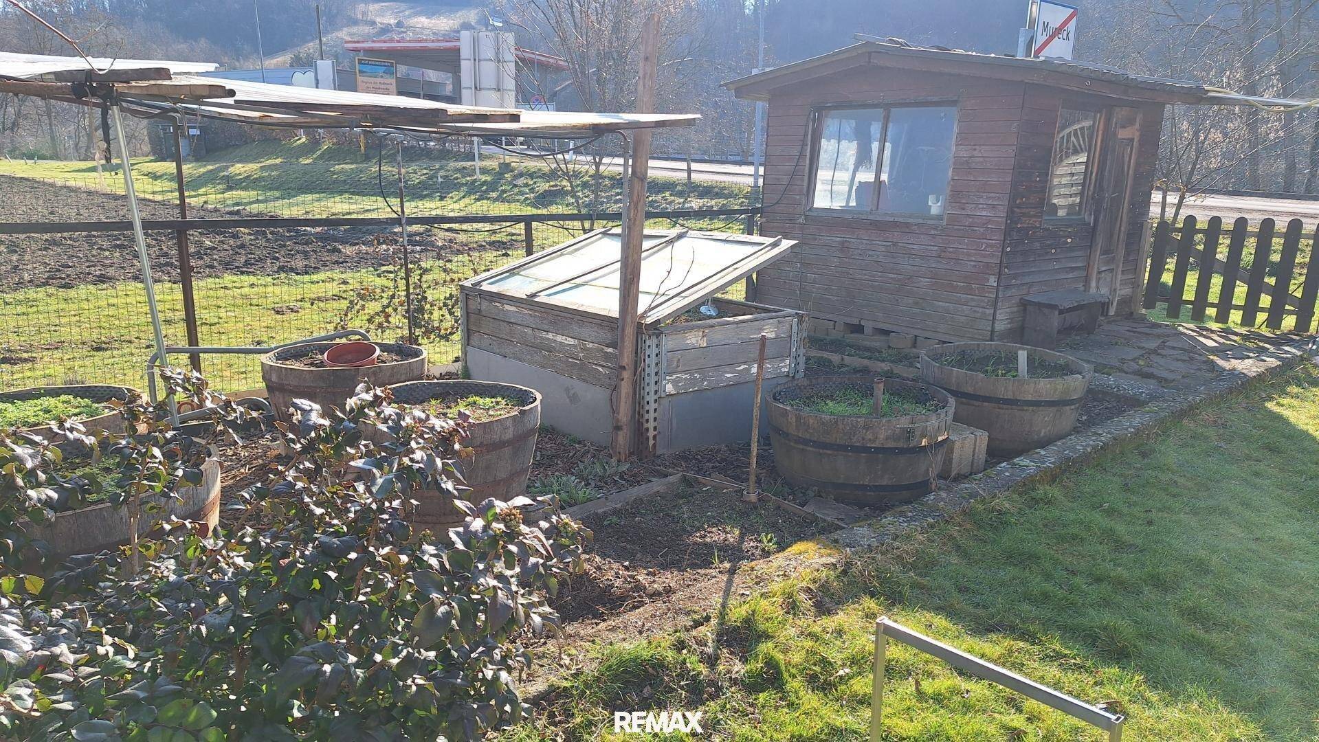 Gartenbereich mit einem kleinen Holzschuppen, Hochbeeten und grüner Wiese.